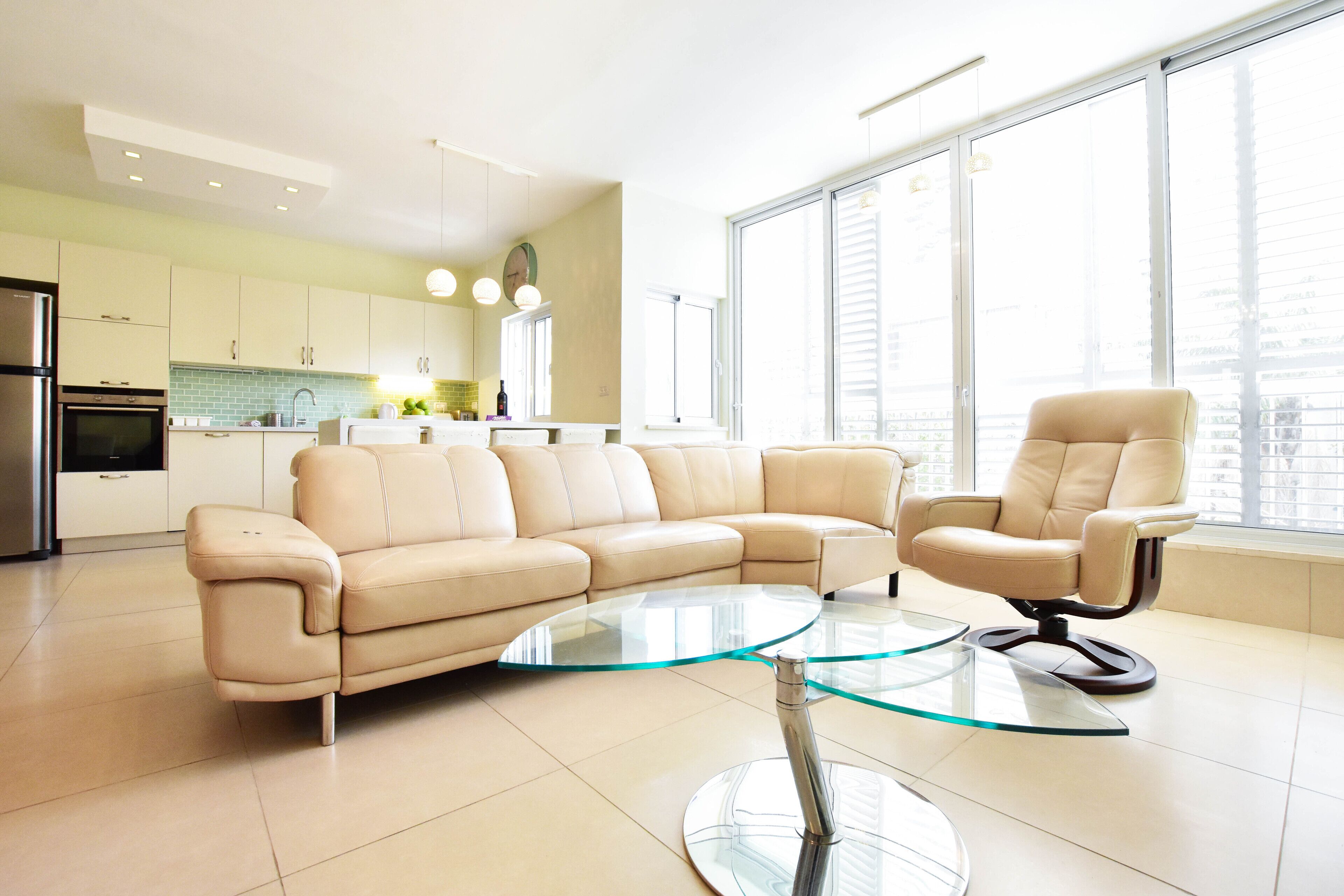 Un salon moderne avec un canapé beige, une table basse en verre et un fauteuil en cuir.