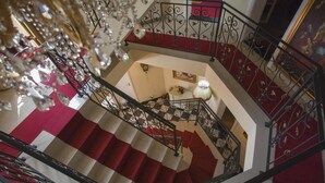 A grand staircase with red and white steps, ornate metal railings, and a chandelier.
