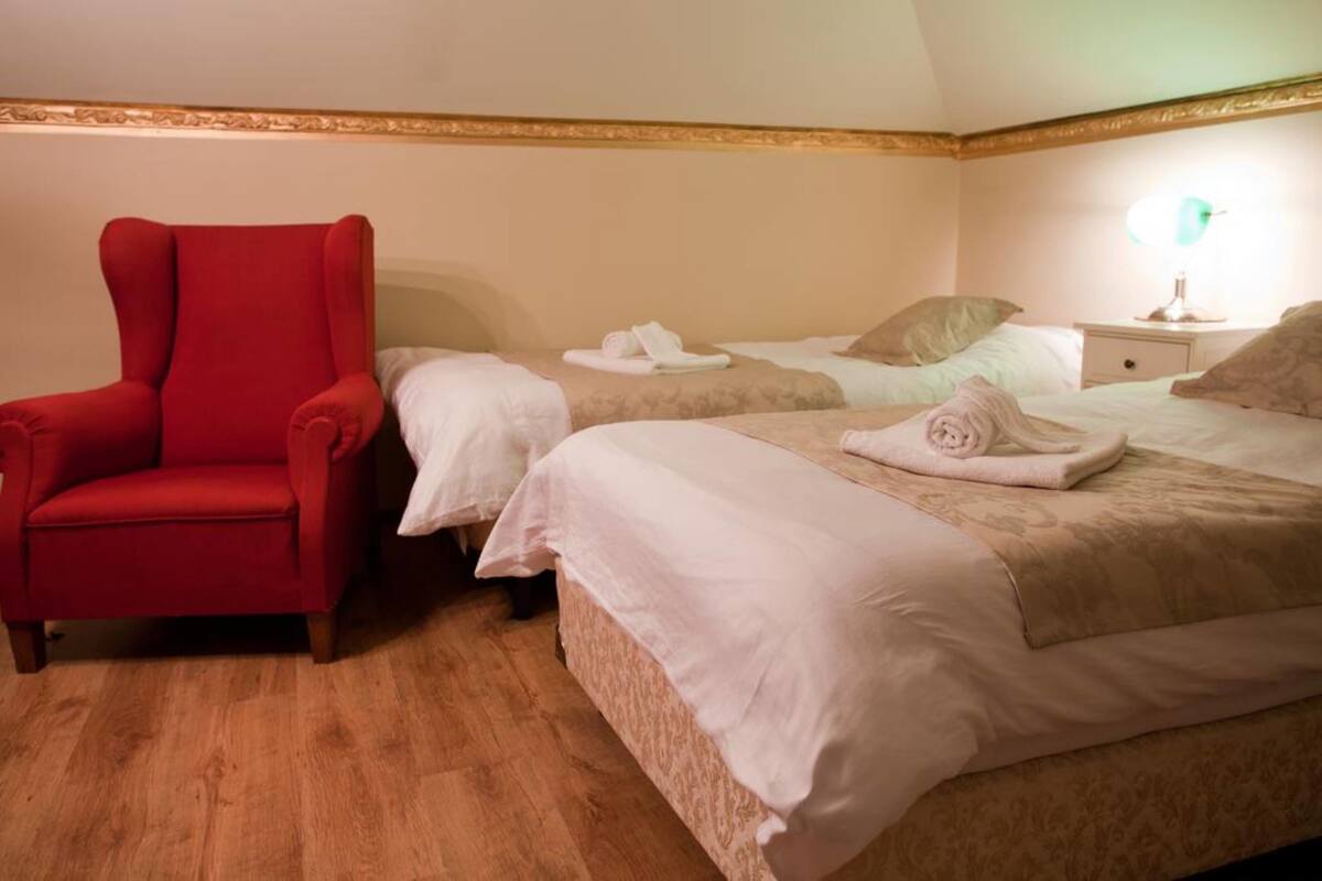 A hotel room with two beds, a red armchair, and a bedside table with a lamp.