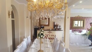A banquet hall with a long table set for a formal event, a chandelier, and a mirror on the wall.