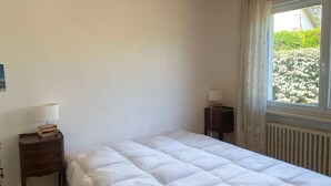 Ein Schlafzimmer mit einem großen Bett, einem Nachttisch mit Lampe, einem Fenster mit Vorhängen und einer Pendelleuchte.