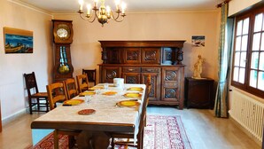 Ein Esszimmer mit einem langen Tisch, gedeckt für sechs Personen, umgeben von Holzsesseln. Dahinter befindet sich eine große Holzkabinet mit aufwendigen Schnitzereien.