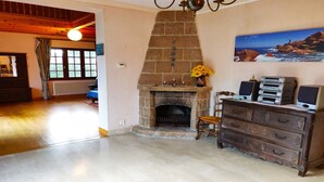 Ein geräumiges Wohnzimmer mit Kamin aus Stein, einer Holzkommode mit elektronischen Geräten und einem Gemälde einer felsigen Küste.