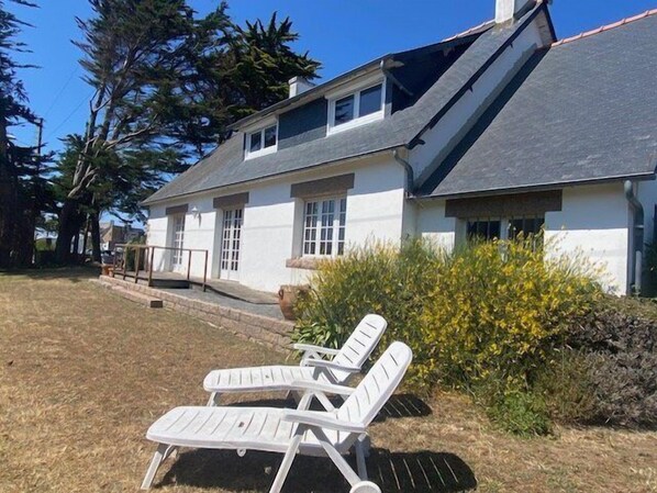 Een tweelaags huis met een schuin dak, witte buitenmuren en een klein terras met een hekwerk.