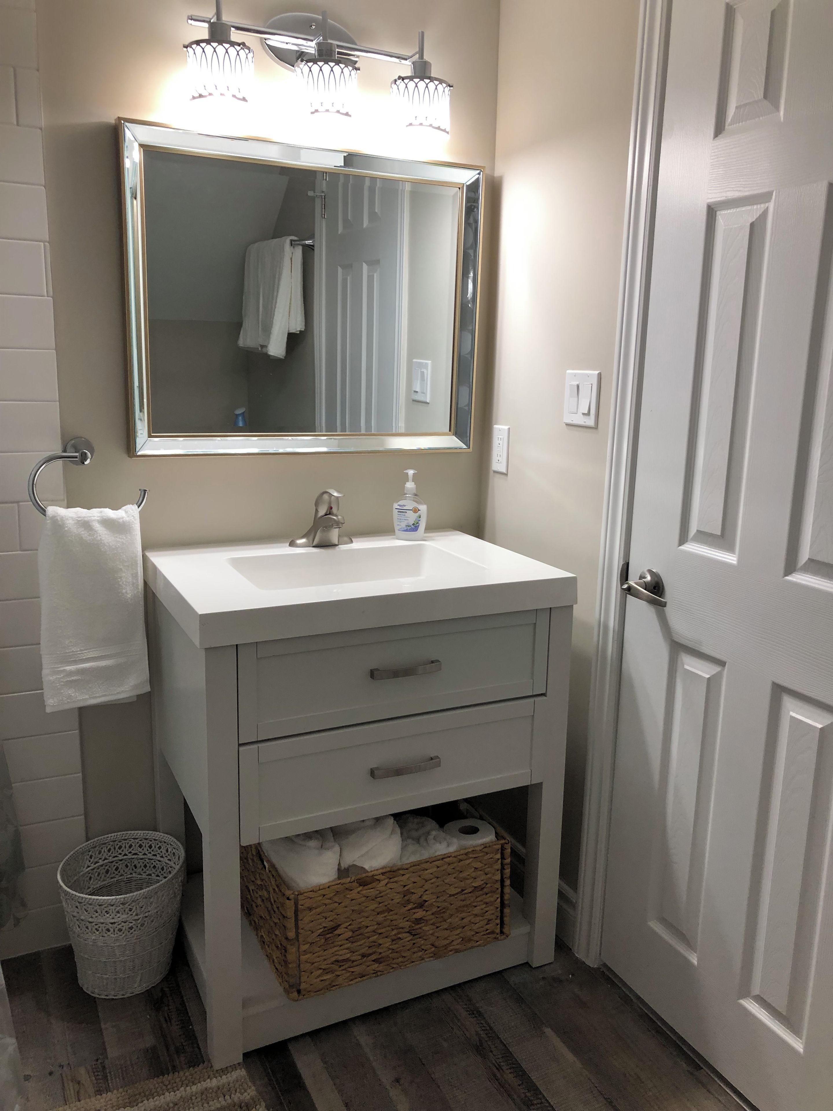A bathroom with a white sink, a mirror, a towel rack, a basket, and a door.