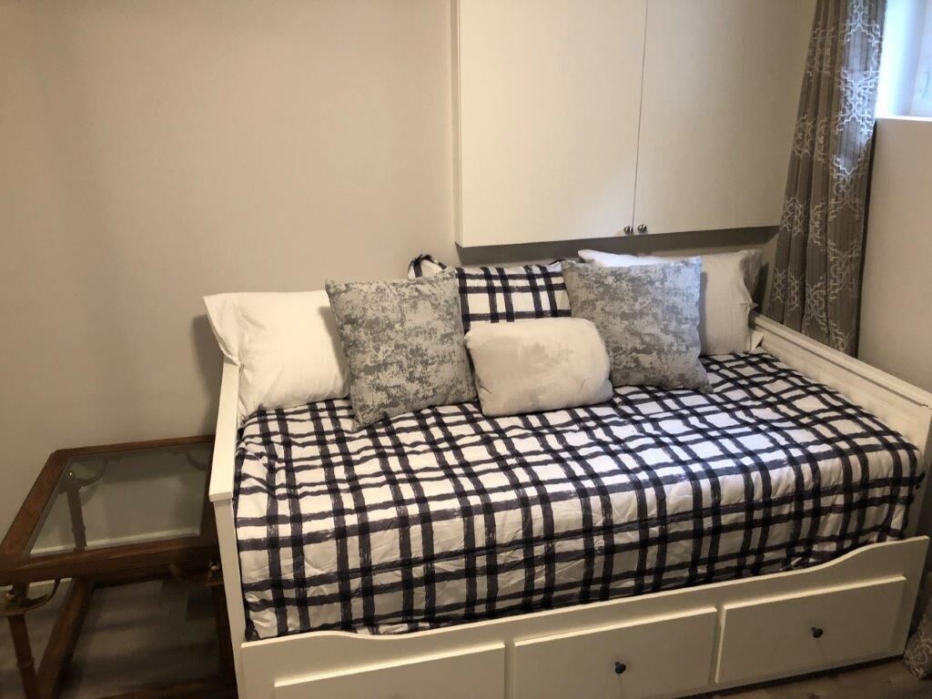 Een bed met een geruit beddegoed, een nachtkastje en een kledingkast in een kamer met effen muren.