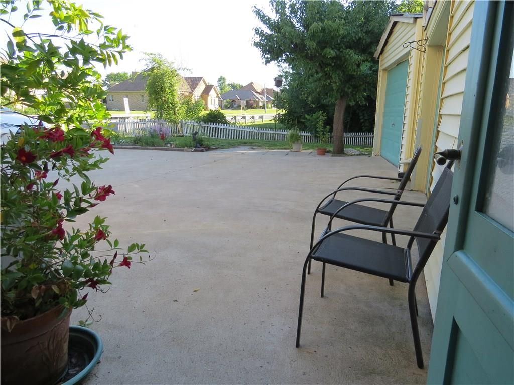 A covered outdoor area with a concrete floor, two metal chairs, and a potted plant with red flowers.