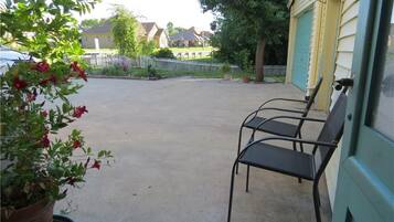 A covered outdoor area with a concrete floor, two metal chairs, and a potted plant with red flowers.