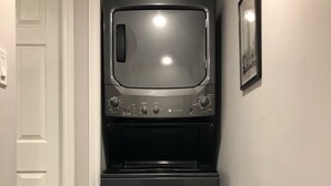 Uma cozinha compacta com forno embutido e micro-ondas, uma porta branca e um quadro pendurado na parede.