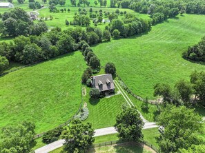 A large, open grassy area with a single house surrounded by trees and a fence.