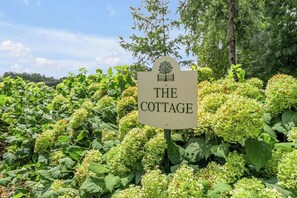 Une enseigne portant l’inscription « THE COTTAGE », entourée d’une végétation luxuriante.