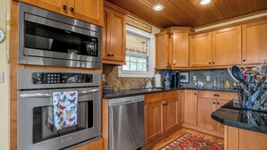 A kitchen with wooden cabinets, stainless steel appliances, and a window with a view. - Orchard Park cottage (Versailles)