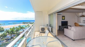Un balcón con vista a la playa, un sofá, un televisor y un equipo de aire acondicionado.