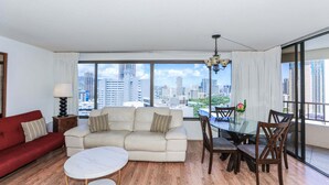 Ein Wohnzimmer mit einer Couch, einem Esstisch, Stühlen, einer Lampe und Blick auf eine Stadtlandschaft durch große Fenster.