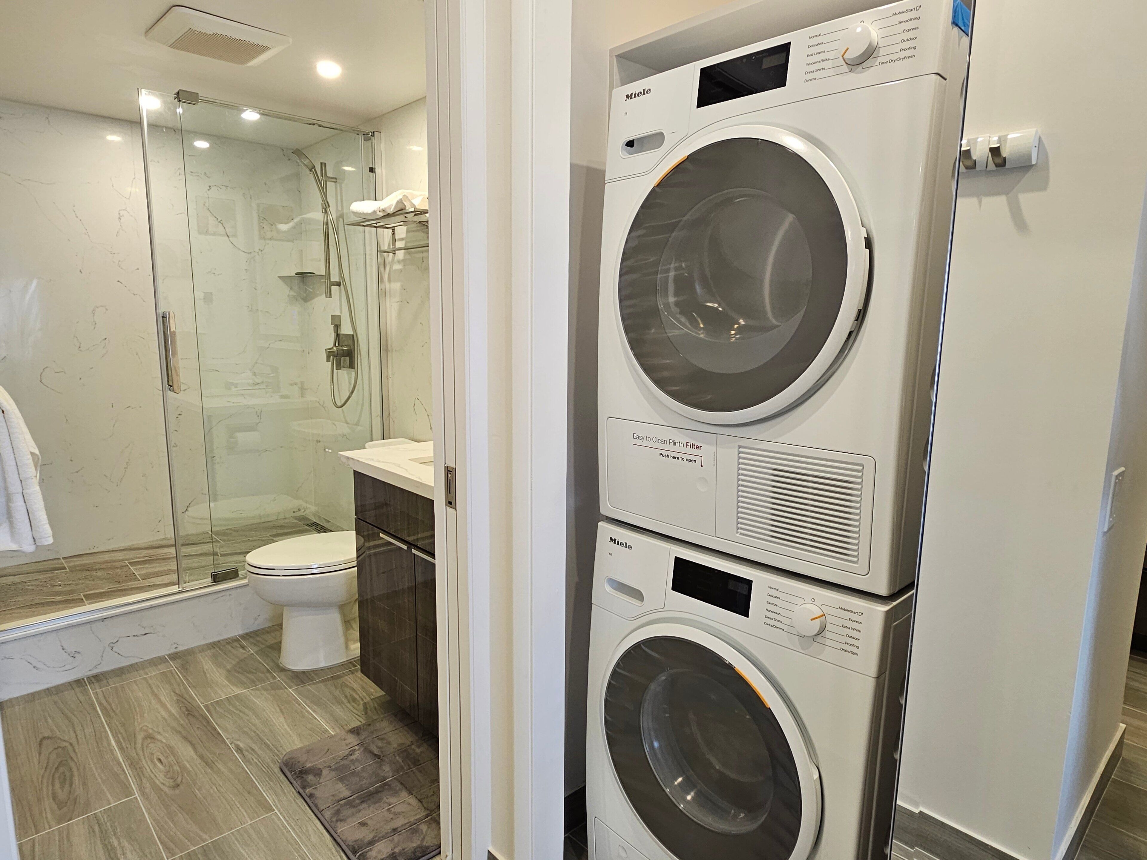 A modern bathroom with a glass-enclosed shower, a toilet, and a stacked washer and dryer.