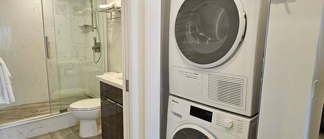 A modern bathroom with a glass-enclosed shower, a toilet, and a stacked washer and dryer.