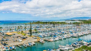 A marina with numerous boats docked, a parking area, and a view of the ocean and distant mountains. - Great Ocean View At The Ilikai Hotel! (Honolulu)