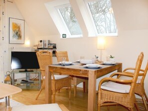 Ruokailutilassa on puinen pöytä, punottuista materiaaleista valmistetut tuolit, televisio ja kirjahylly.