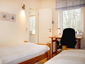 Habitación con dos camas, un escritorio, una silla y ventana con vista a árboles.