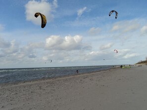 Una spiaggia con persone che fanno volare aquiloni e una struttura gonfiabile verde sulla sabbia.