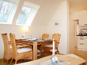 A dining area with a wooden table, wicker chairs, a candle, and a kitchen in the background. - Barendorf apartment Föllenbach (Dassow)