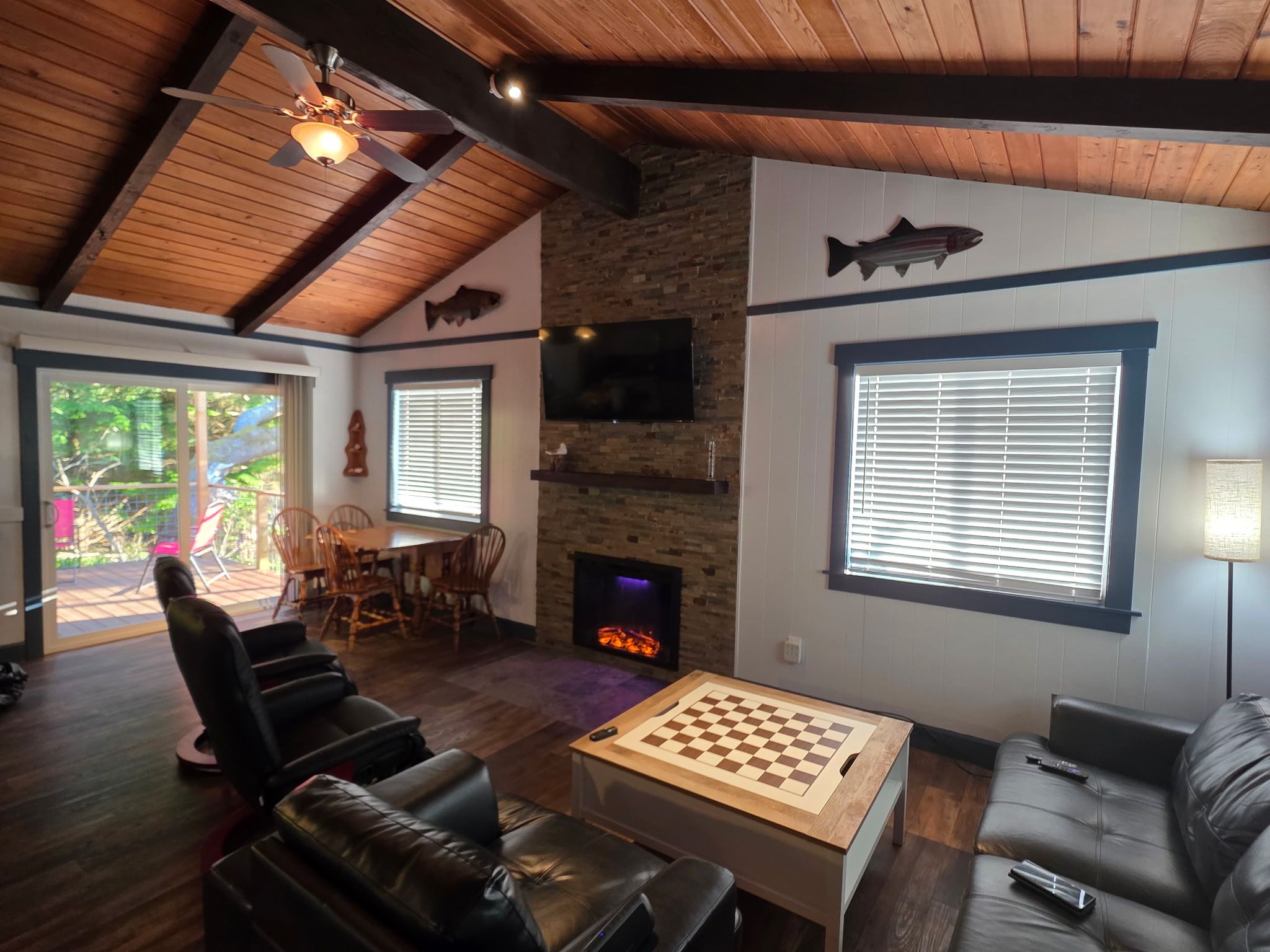 Un salon chaleureux avec une cheminée, un décor mural représentant des poissons, une table d’échecs et des sièges confortables.