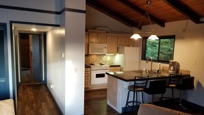 A modern kitchen with wooden cabinets, a central island with bar stools, and a large window. - Cute Rockaway Beach Cabin (Rockaway Beach)