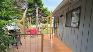 A wooden deck with a grill and red chairs, a fenced area, and a building with a window and door. - Cute Rockaway Beach Cabin (Rockaway Beach)
