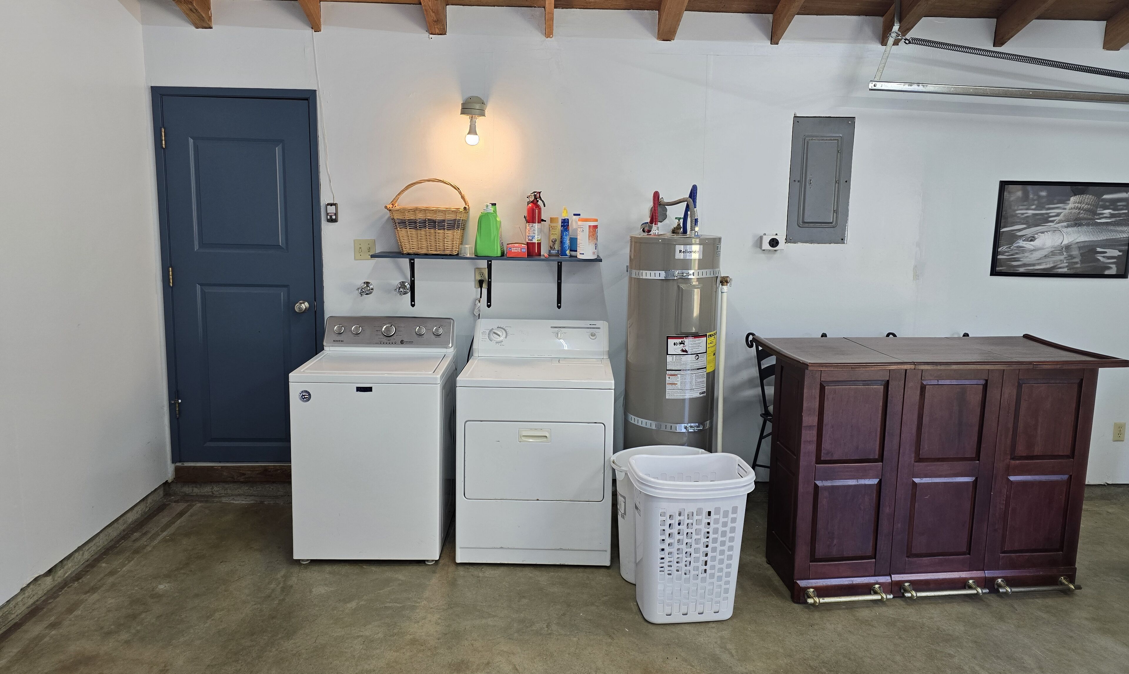 A laundry room with two washing machines, a dryer, a water heater, and a wooden cabinet.