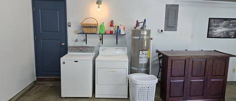 A laundry room with two washing machines, a dryer, a water heater, and a wooden cabinet.