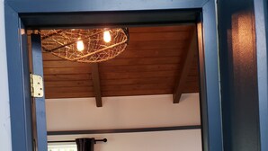 A room with a bunk bed, a wooden ceiling, a window with curtains, and a wall-mounted light fixture. - Cute Rockaway Beach Cabin (Rockaway Beach)