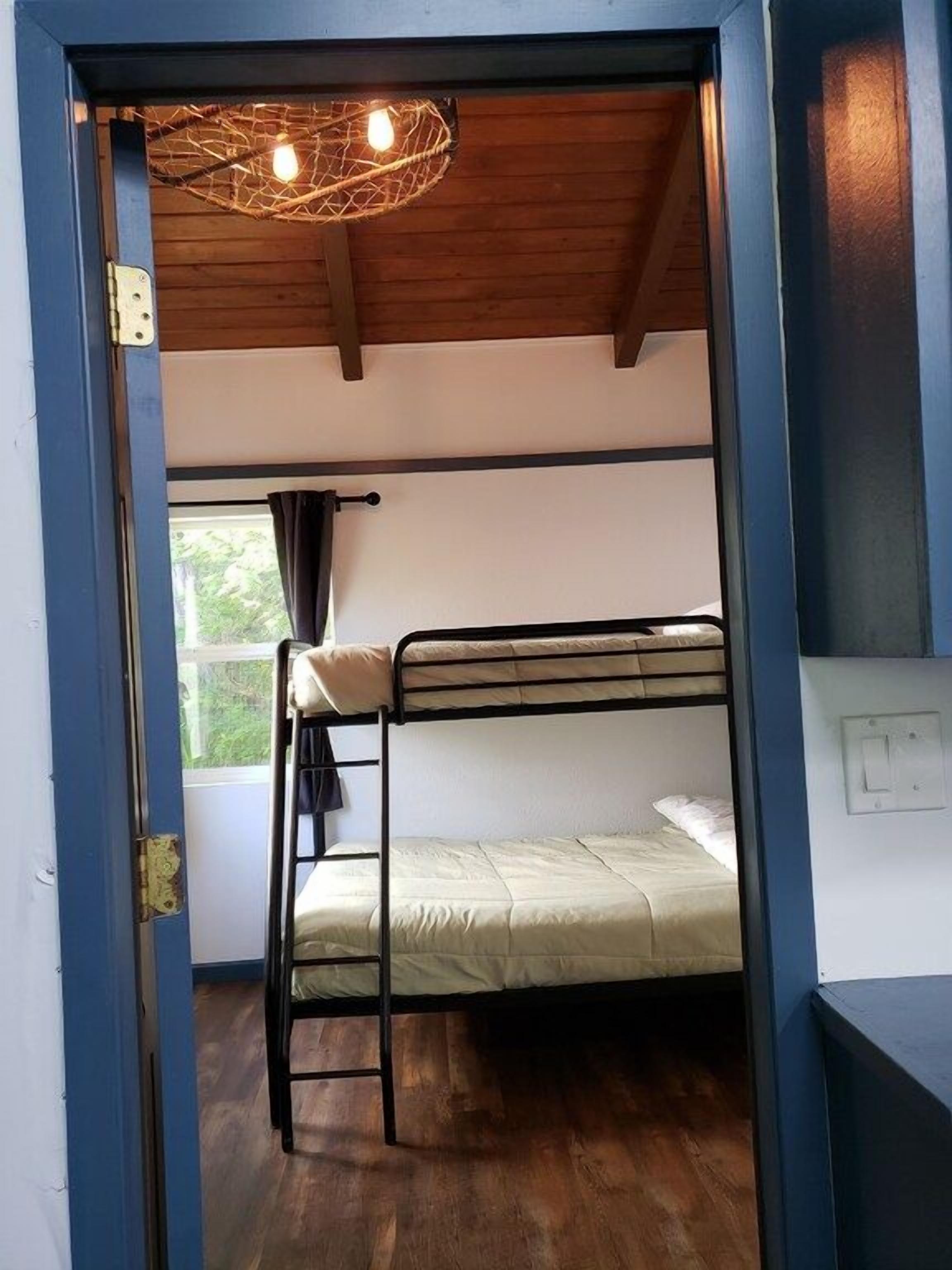 A bunk bed room with a wooden ceiling and a window with curtains.