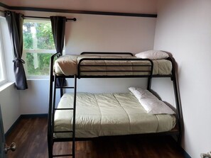 A bunk bed with a window and curtains, a wooden floor, and a door with a handle. - Cute Rockaway Beach Cabin (Rockaway Beach)