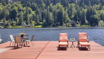 Relax on the lakeside deck with lounge chairs and a table, surrounded by a dense forest and serene water.