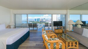 Une chambre d’hôtel avec un lit, un canapé, une table à manger et un téléviseur. Elle dispose d’un balcon avec vue sur la ville et l’océan.