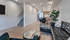 Una sala de estar moderna con un sofá de cuero, una mesa de centro de vidrio y una escalera que lleva a una zona de cocina.
