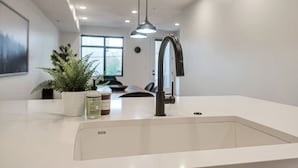 Una cocina moderna con encimera blanca, grifo negro, una planta en maceta y una taza de café.