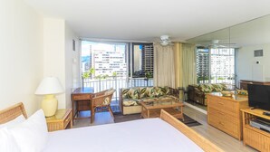 A hotel room with a bed, a sofa, a TV, a balcony with a view of buildings, and a ceiling fan. - Charming Ilikai Marina Studio, Great Location In Waikiki! (Honolulu)