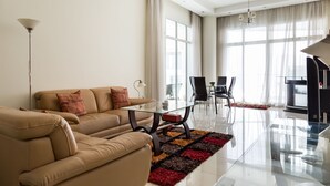 Ein modernes Wohnzimmer mit einem beigen Sofa, einem Glastisch und einem Essbereich mit Tisch und Stühlen.