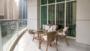 Ein Balkon mit Korbmöbeln, einem Glastisch und Blick auf einen Fluss sowie hohe Gebäude.
