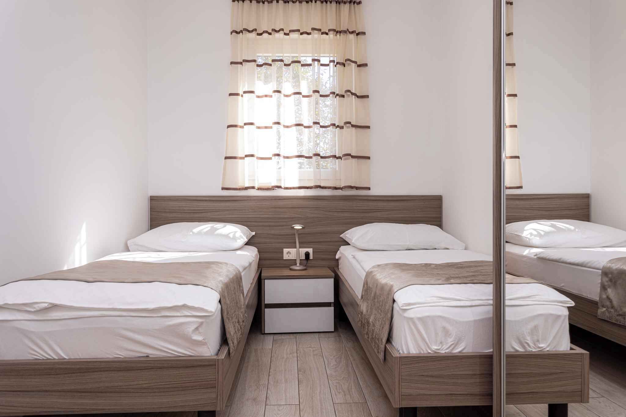 Ein Schlafzimmer mit zwei Einzelbetten, einem Nachttisch mit Lampe und einem Fenster mit durchsichtigem Vorhang.