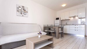 Una sala de estar moderna con un sofá, una mesa de centro y un comedor con sillas, y una cocina al fondo.