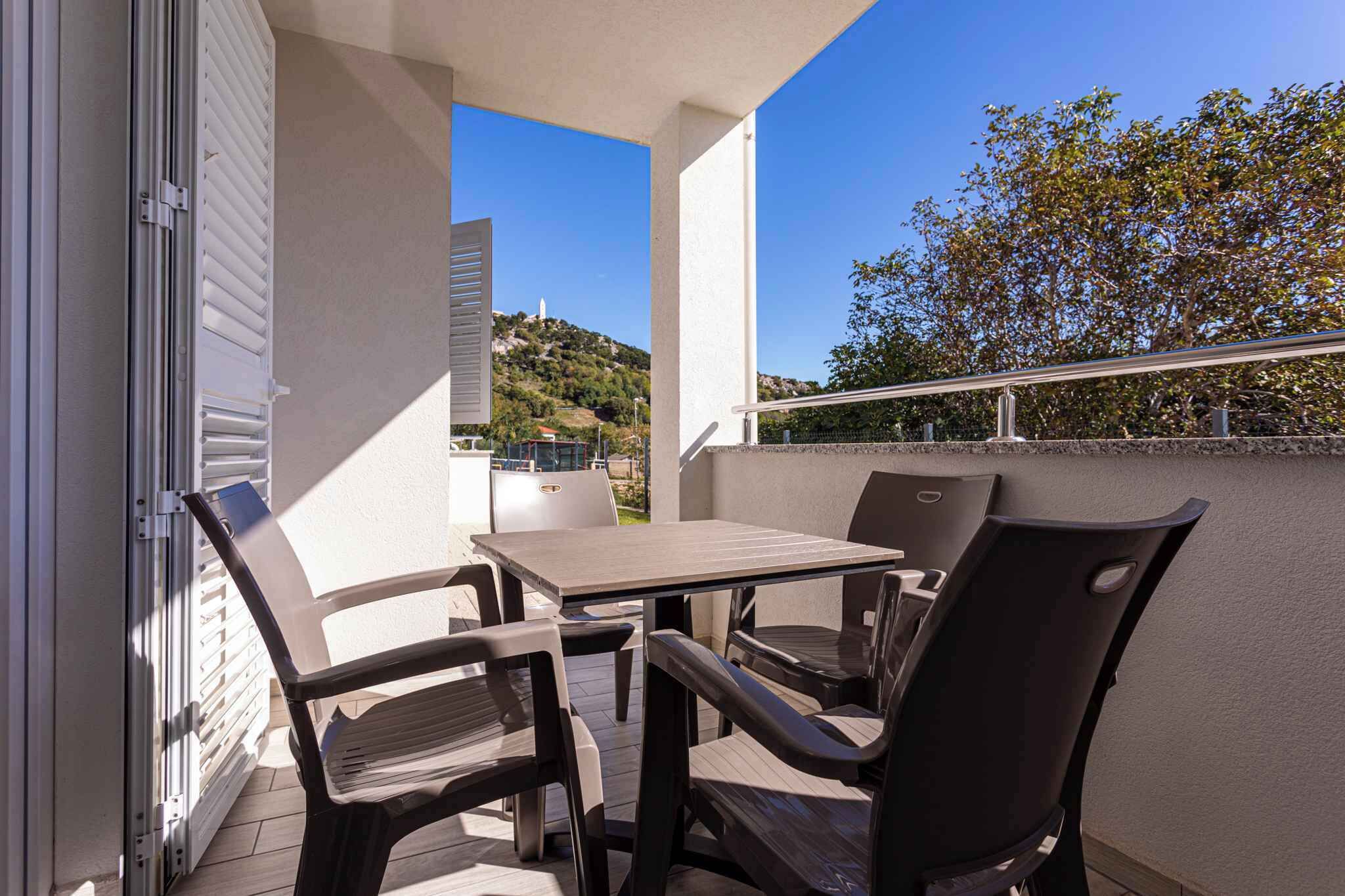 Ein Balkon mit Tisch und Stühlen, Geländer und Blick auf einen Hügel mit Gebäuden.