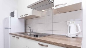 Una cocina moderna con armarios blancos, un lavamanos de acero inoxidable, un microondas y un hervidor sobre la encimera.