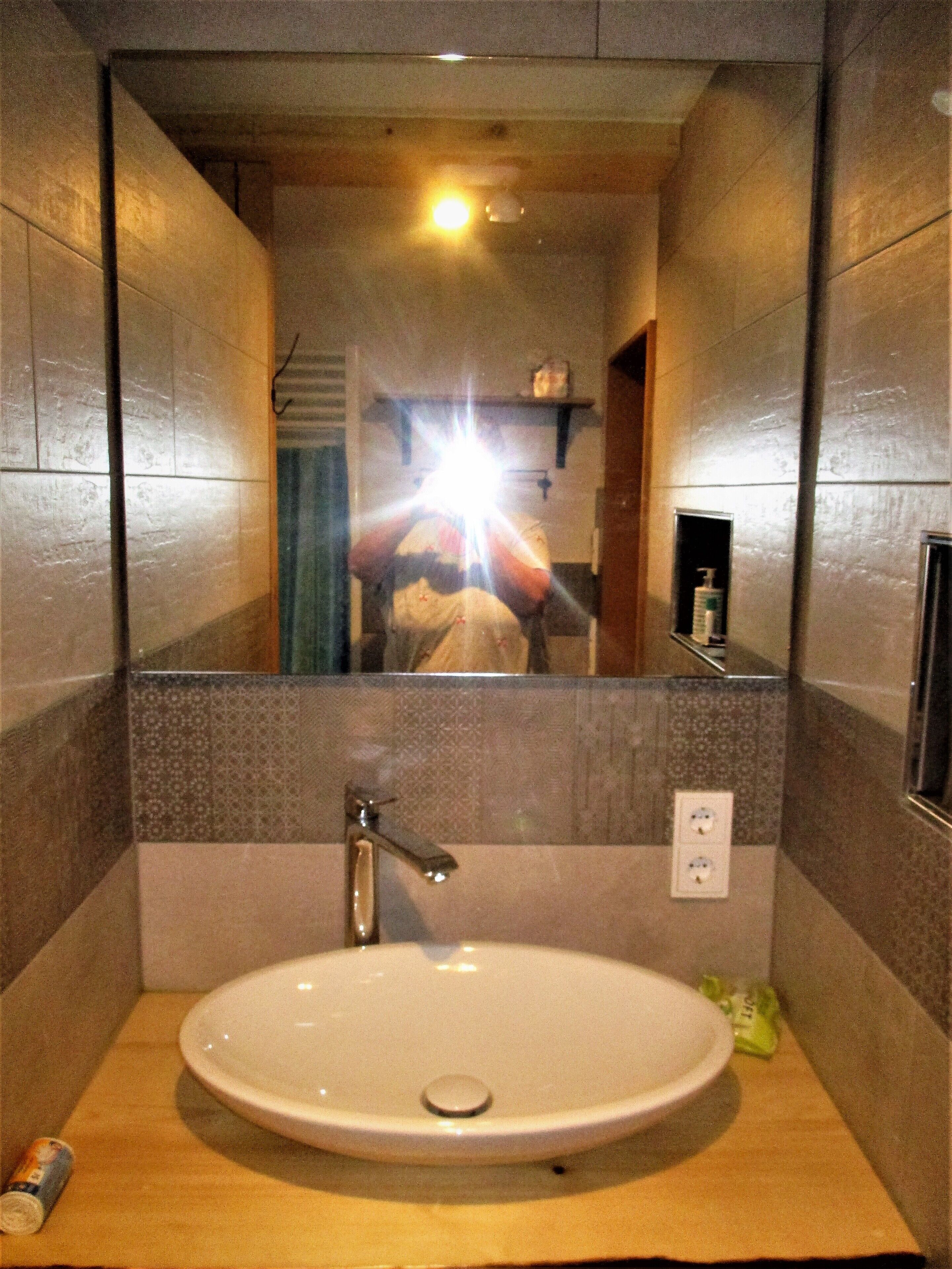 A bathroom with a sink, mirror, and a bottle of hand soap on the wall.