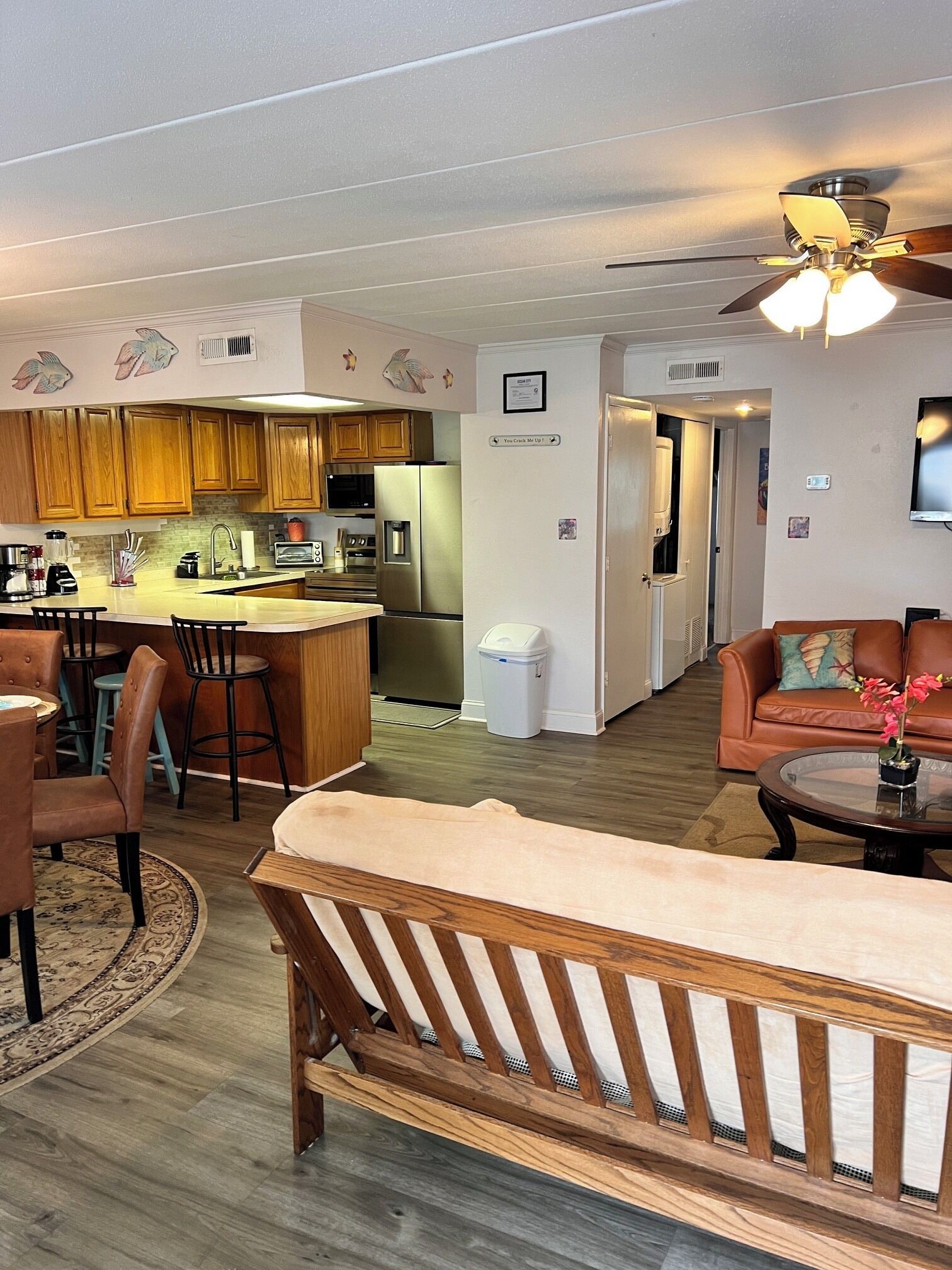 A modern kitchen with wooden cabinets, a central island, and a dining area with chairs and a sofa.