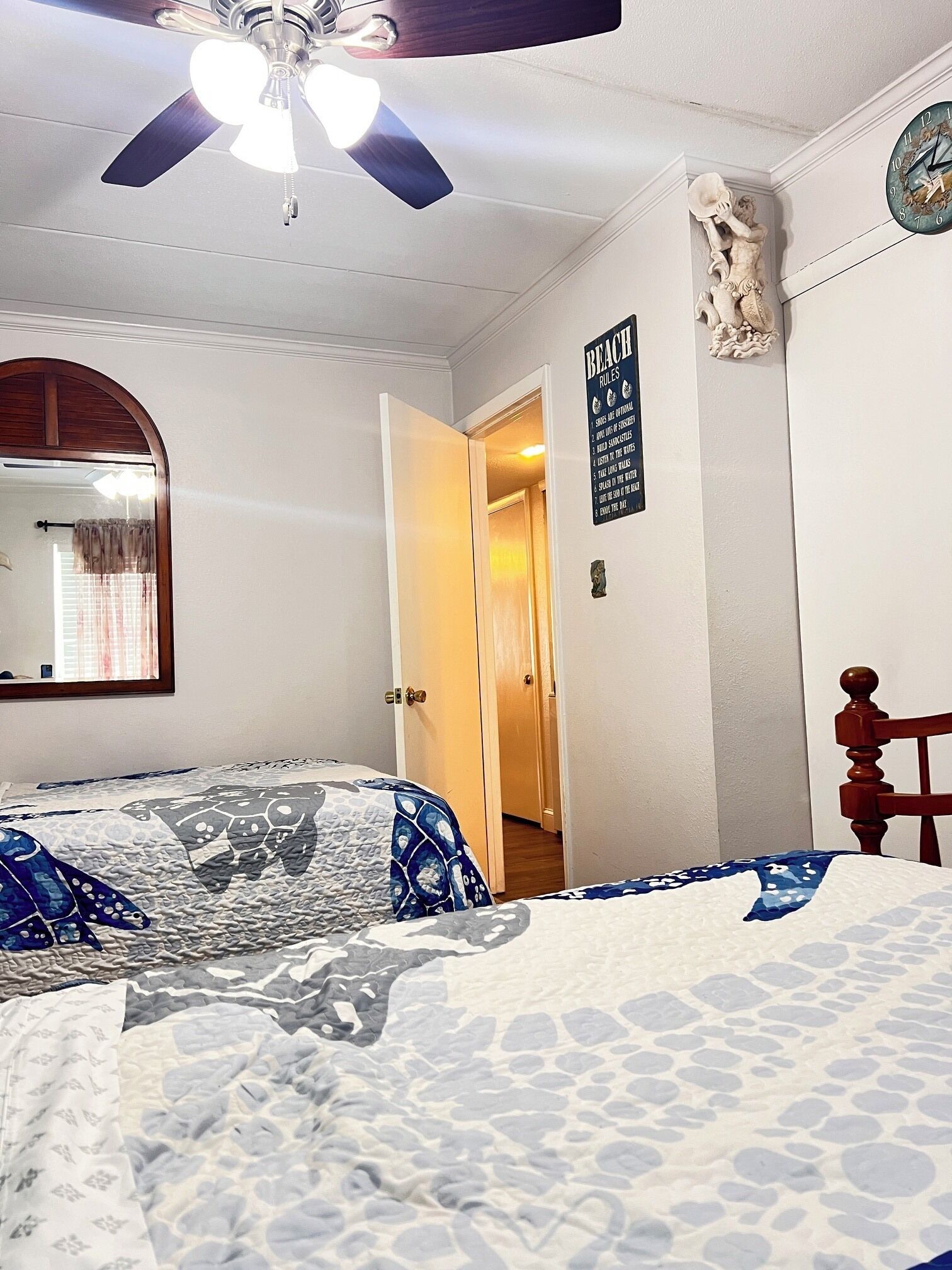 Een slaapkamer met een bed, een plafondventilator, een klok, een deur en een bord aan de muur.