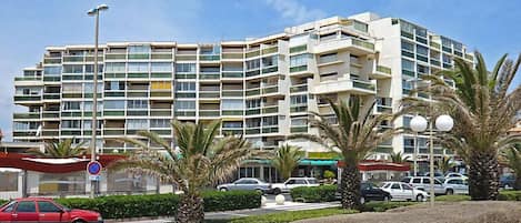 A multi-story hotel with balconies, a parking area, and palm trees.