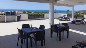 Een terras op het dak met buitenmeubilair, een tafel en uitzicht op de oceaan.