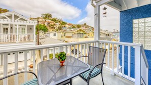 Un balcon avec une table et des chaises en métal, un pot de fleurs et une vue sur des maisons colorées situées sur une colline.